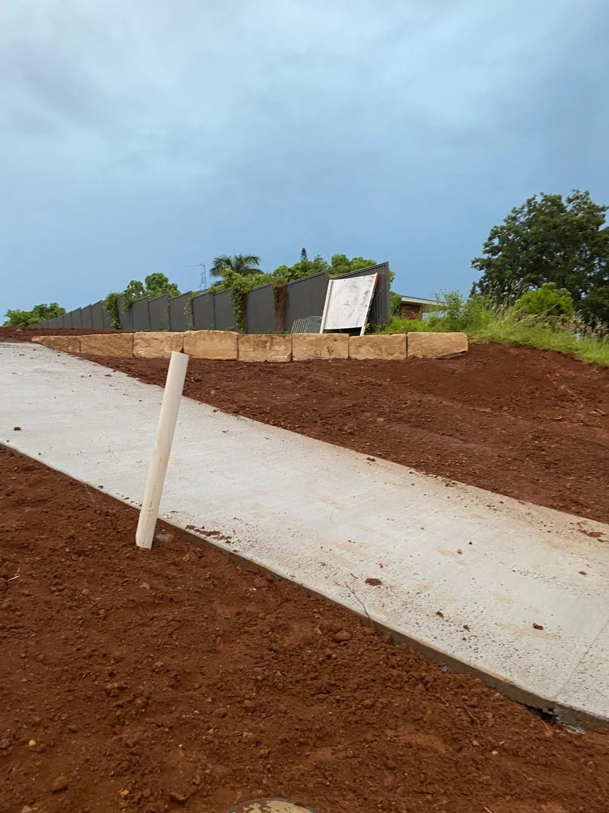 Concrete path below a sandstone wall and a metal fence